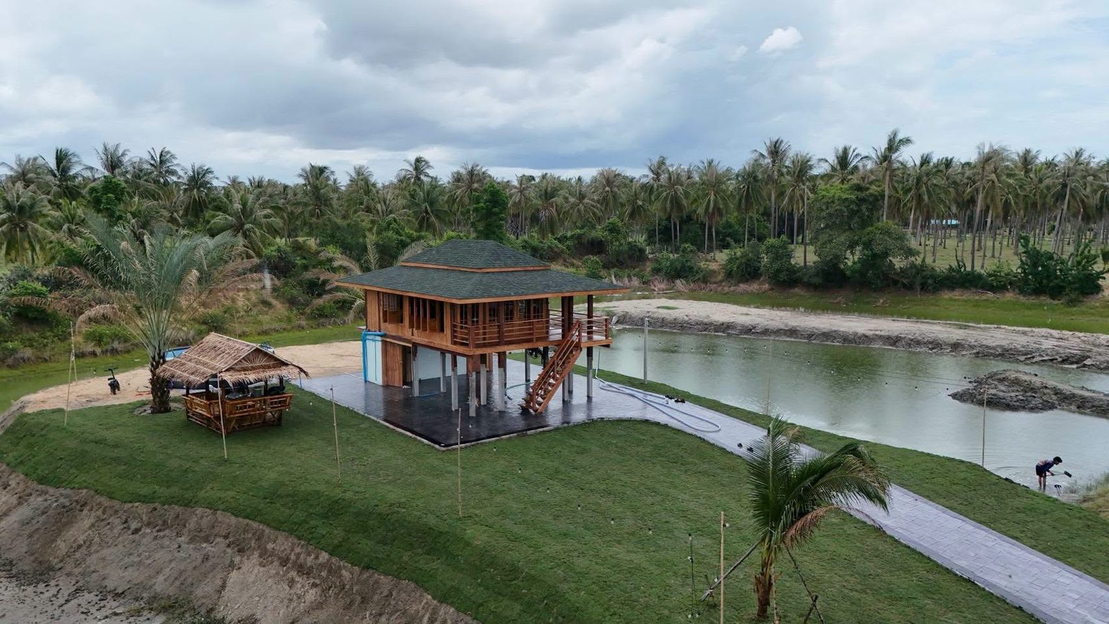 The finished teak house of The Nine with its veranda and lawn in Kui Buri, Thailand